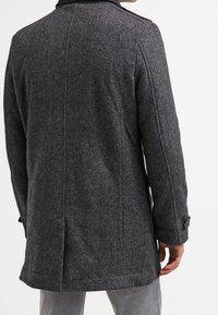 Cappotto in lana grigio carbone con un design strutturato, caratterizzato da un collo alto e dettagli con bottoni sulle maniche, mostrato da dietro.