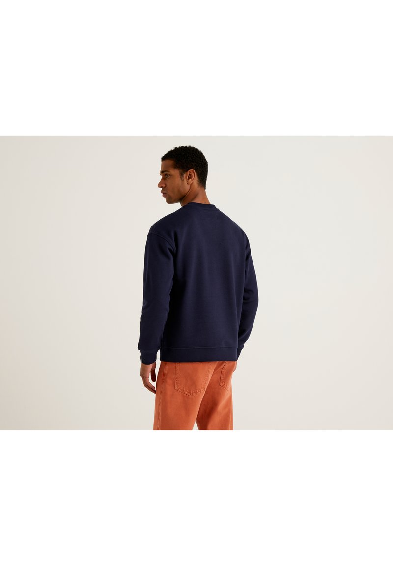 Sudadera de cuello redondo en azul marino con puños y dobladillo acanalados, combinada con pantalones naranjas. La tela parece suave y de peso pesado.
