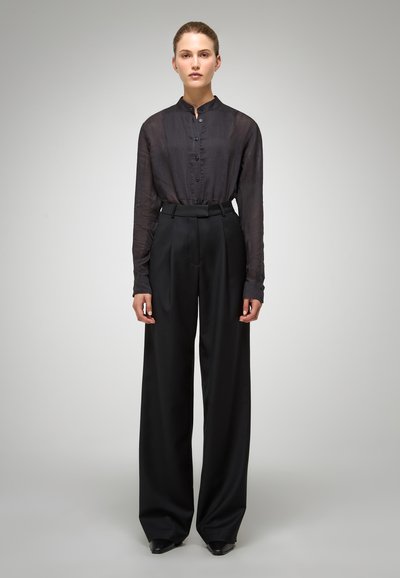 Blouse noire à manches longues et boutonnée en tissu transparent, associée à un pantalon large noir taille haute. Les deux présentent une finition élégante.