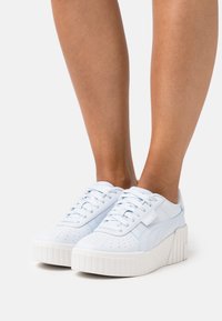 Baskets blanches et bleu clair à lacets, avec une tige en cuir texturé, des détails perforés et une semelle blanche épaisse et rainurée.