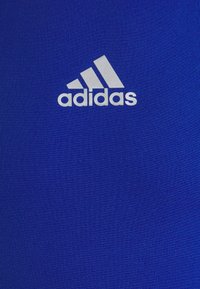 Blauw sporthemd van gladde stof met een witte Adidas-logo centraal op de borst.