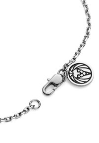 Silver chain bracelet with a lobster clasp and a round pendant featuring an intricate black design. Smooth texture, minimalist style.