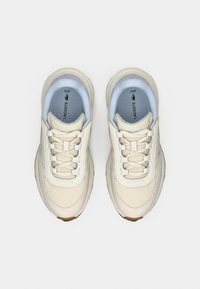 Αθλητικά παπούτσια Lacoste σε κρεμ χρώμα με ανοιχτογάλαζες λεπτομέρειες. Διαθέτουν υφασμένο επάνω μέρος, στρογγυλή μύτη και επίπεδα κορδόνια. Ορατό πάτο Ortholite®.