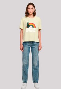 Yellow cotton t-shirt featuring a graphic with trees and a rainbow, text reads "DESTROY THE PATRIARCHY NOT THE PLANET," paired with light blue jeans.