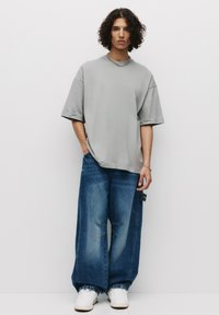 Lichtgrijze oversized t-shirt gecombineerd met losse blauwe denim jeans met versleten accenten. Witte sneakers maken de outfit compleet.