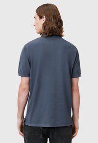 Marinblå pikétröja med korta ärmar, tillverkad av mjukt tyg. Har en avslappnad passform och sidoklipp vid nederkant för ökad rörelsefrihet.