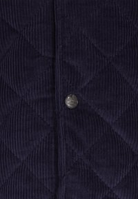 Marinblå quilted corduroy tekstil med diagonale ribber og en metallknap i midten, der tilføjer en detalje til designet.