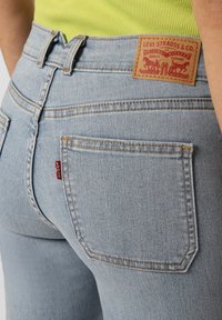 Vaqueros de mezclilla azul claro con cintura alta, que cuentan con bolsillos traseros, costuras amarillas y un parche de cuero de Levi Strauss en la cintura.