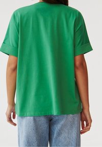 Camiseta verde de manga corta con un corte holgado, escote redondo y puños enrollados, hecha de una tela suave con una textura lisa.