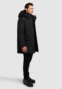 Black insulated parka with a hood, zip closure, front pockets, and a relaxed fit. Features a smooth, matte texture and minimal detailing.