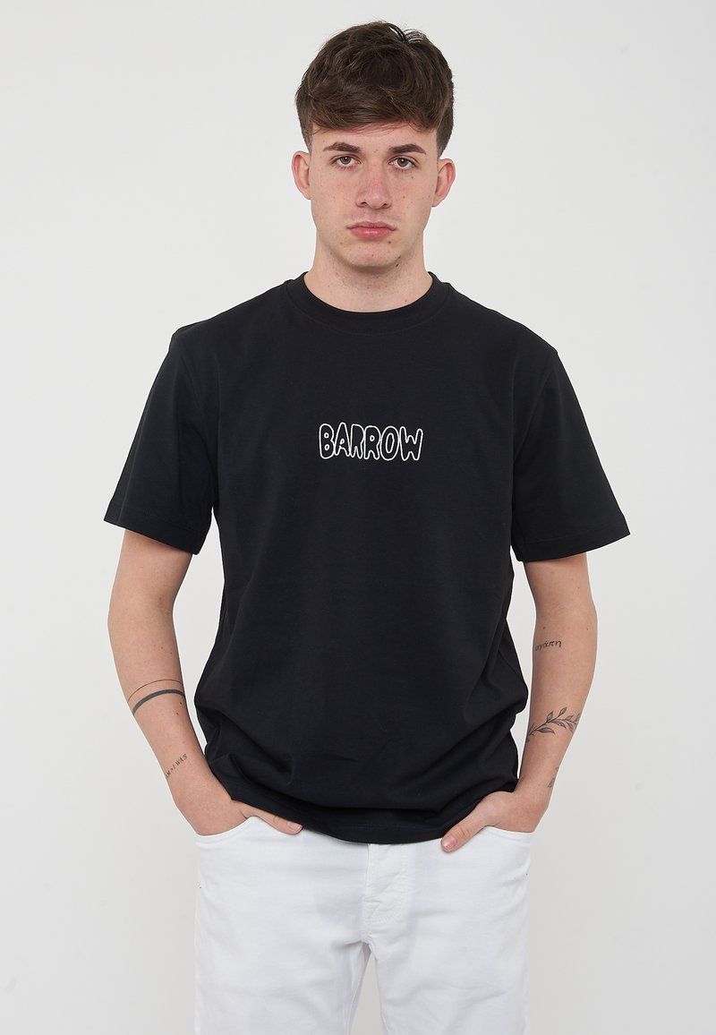 T-shirt nera in cotone con scollatura rotonda, maniche corte e testo ricamato in bianco "BARROW" sul davanti. Indossata con pantaloni bianchi.