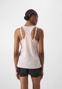 Lys rosa treningstopp med scoop-back-design og justerbare stropper, kombinert med svarte shorts. Stoffet ser glatt og stretchy ut.