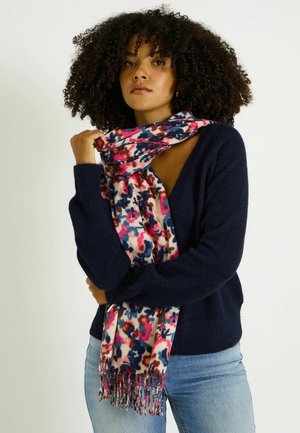 Écharpe à imprimé floral multicolore aux tons roses et bleus, bords frangés, portée sur un pull bleu marine. Tissu doux, design léger.