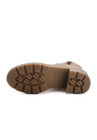 Bota de ante en tono marrón claro con una suela de goma texturizada que presenta un patrón en relieve para un mejor agarre. Cierre lateral con cremallera y diseño de punta redonda.