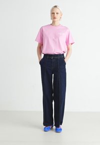 Ružičasta pamučna majica s ispisanim tekstom, uparen s tamnoplavim trapericama visokog struka koje imaju pojas. Plave cipele zaokružuju ovaj outfit.