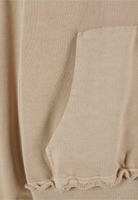 Tissu de sweat-shirt beige avec une poche et un ourlet à volants. Texture lisse avec un motif tricoté subtil.