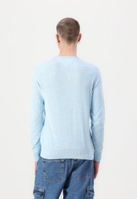 Svetlo modri pleteni pulover z dolgimi rokavi, subtilno teksturo in dekoltejem v obliki črke V. Nosi se z denim udobnimi hlačami.