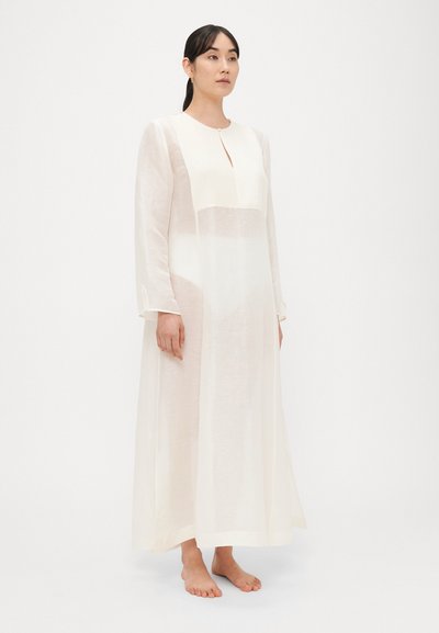 Μακρύ, διαφανές λευκό φόρεμα με στρογγυλή λαιμόκοψη, μπροστινή λεπτομέρεια με άνοιγμα και μακριά μανίκια. Διαθέτει άνετη εφαρμογή και απαλή, ελαφριά ύλη.