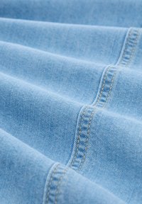 Lichtblauwe denimstof met zichtbare stiksels in een contrasterend geel. Vouw met een gladde textuur en een lichte glans.