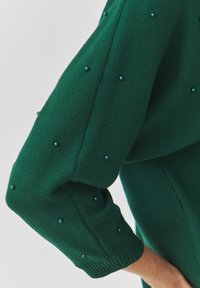 Maglione verde a maglia con maniche lunghe, caratterizzato da perline decorative color turchese lungo le maniche. Morbido al tatto e con dettagli a coste sui polsini.