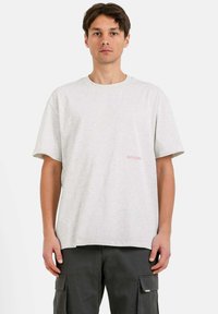 Camiseta de manga corta gris hecha de algodón, con un pequeño logo rosa en el pecho. El corte es relajado con hombros caídos.