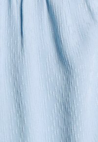 Tissu bleu clair avec un motif texturé. Le matériau semble lisse avec un léger éclat, mettant en valeur des designs complexes, légèrement en relief.