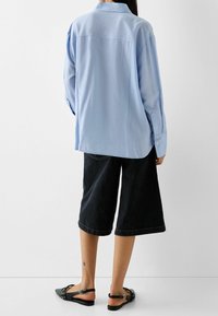 Ljust blå långärmad skjorta i mjukt tyg, med knäppbara manschetter, kombinerad med svarta denimculottes och svarta slingback-sandaler med nitar.