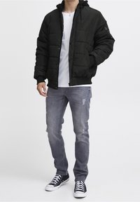 Czarna pikowana kurtka puchowa z kapturem, z przeszywanym wzorem i ściągaczami na mankietach, w połączeniu z bia�łym t-shirtem oraz szarymi podniszczonymi jeansami, uzupełniona czarnymi trampkami.