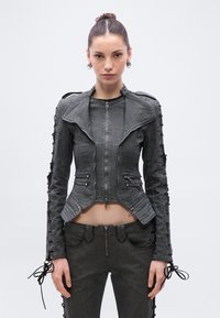 Tumesinise tooni teksast mootorrattajaki lameda lõikega, esiküljel lukuga ning varrukaatel pitsiäärtega; koos sobivate pükstega.