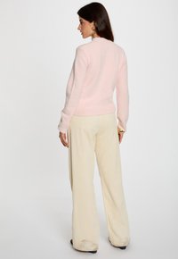 Helles rosa Pullover mit rundem Halsausschnitt und langen Ärmeln, kombiniert mit weiten Beigefarbenen Cordhosen. Weicher, strukturierter Stoff.