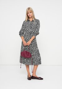 Μαύρο και άσπρο φόρεμα με ρίγες ζέβρας, μακριά μανίκια και κλειστή μέση, συνδυασμένο με μια μπορντό τσάντα και γυαλιστερά καφέ μπαλαρίνα.