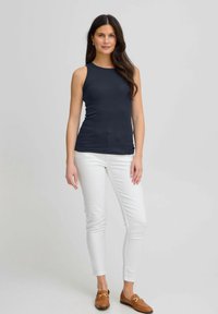 Top sin mangas de color navy, confeccionado en una tela elástica, combinado con jeans skinnies blancos y mocasines marrones, con un ajuste ceñido.