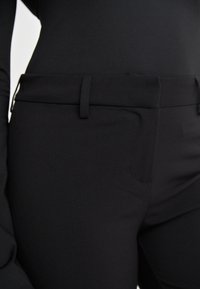 Black tailored pants with a smooth texture, featuring a mid-rise waist, belt loops, and front pockets. Simple design and sleek silhouette.