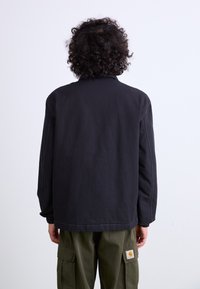 Black lightweight jacket with long sleeves, relaxed fit, and visible stitching details, worn over green cargo pants.