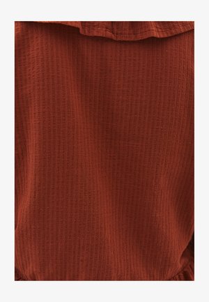 Rust-colored textured fabric featuring a subtle ribbed pattern, with a ruffled neckline and soft, unstructured drape.