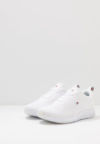 Valkoiset urheilukengät tekstiilipintaisella raidallisella yläosalla, nauhakiinnityksellä ja kuviolteisella kumipohjalla. Sisältää pienen logon ja kontrastivärejä.