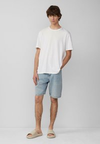 T-shirt en coton blanc, short en denim bleu clair et sandales à enfiler beiges. Tenue décontractée avec une coupe ample et des textures subtiles.