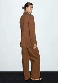 Bruin linnen pak met een lange jas en wijde broekspijpen, met een relaxed fit, subtiele textuur en minimalistisch ontwerp.