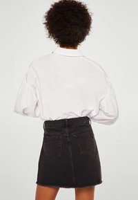Camisa blanca de cuello con mangas abullonadas, combinada con una minifalda de mezclilla negra con dobladillo deshilachado y dos bolsillos traseros.