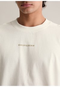 Off-weißer Sweatshirt mit geripptem Rundhalsausschnitt, weichem Stoff und einem zentralen Logo in goldener Schrift: "MARCOPOLODENIM."