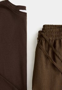 Chemise à manches longues marron foncé à côté d'un pantalon rayé marron avec taille élastique et cordon sur fond clair.