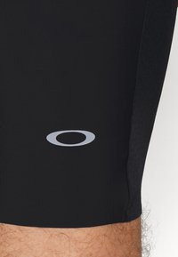 Shorts de sport noirs avec un design épuré, une texture lisse et un logo gris réfléchissant sur la jambe inférieure.