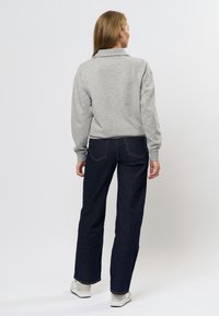 Sivá, mäkká mikina s golierom; kombinovaná s tmavomodrými džínsami s rovnými nohavicami. Osoba je otočená chrbtom, čo ukazuje zadnú časť oblečenia.