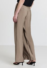 Beige Weitbein-Hosen aus einem glatten, leichten Stoff. verfügen über einen einfachen Bund und seitliche Taschen, kombiniert mit schwarzen Absätzen.