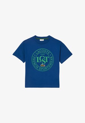 Niebieska koszulka z krótkim rękawem z zielonym okrągłym logo Lacoste Paris French Sportswear oraz małym haftowanym emblematem krokodyla na środku klatki piersiowej.