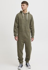 Olive green zip-up onesie made of soft fabric, featuring a hood, front pockets, ribbed cuffs, and a contrasting beige drawstring.