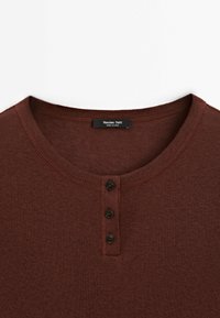 Bruine langarmtop van zachte stof met een ronde hals, voorzien van een drieknoopsluiting en fijne geribbelde afwerking. Merkenlabel zichtbaarheid.