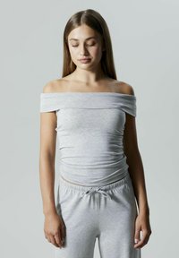 Grå av-shoulder topp med en tettsittende design, laget av myk, elastisk stoff. Strukturert, rynket detalj ved midjen. Kombinert med grå bukser.