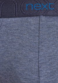 Graue Stoff-Boxershorts mit glatter Textur, ausgestattet mit einem dunklen Taillenbund, auf dem das erhobene "next"-Logo in Blau prangt.