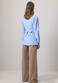 Világoskék, gombos ing nyakkendő hátsó résszel, bézs, bő szárú nadrággal párosítva. Hosszú ujjai és egyenes fazonja van.